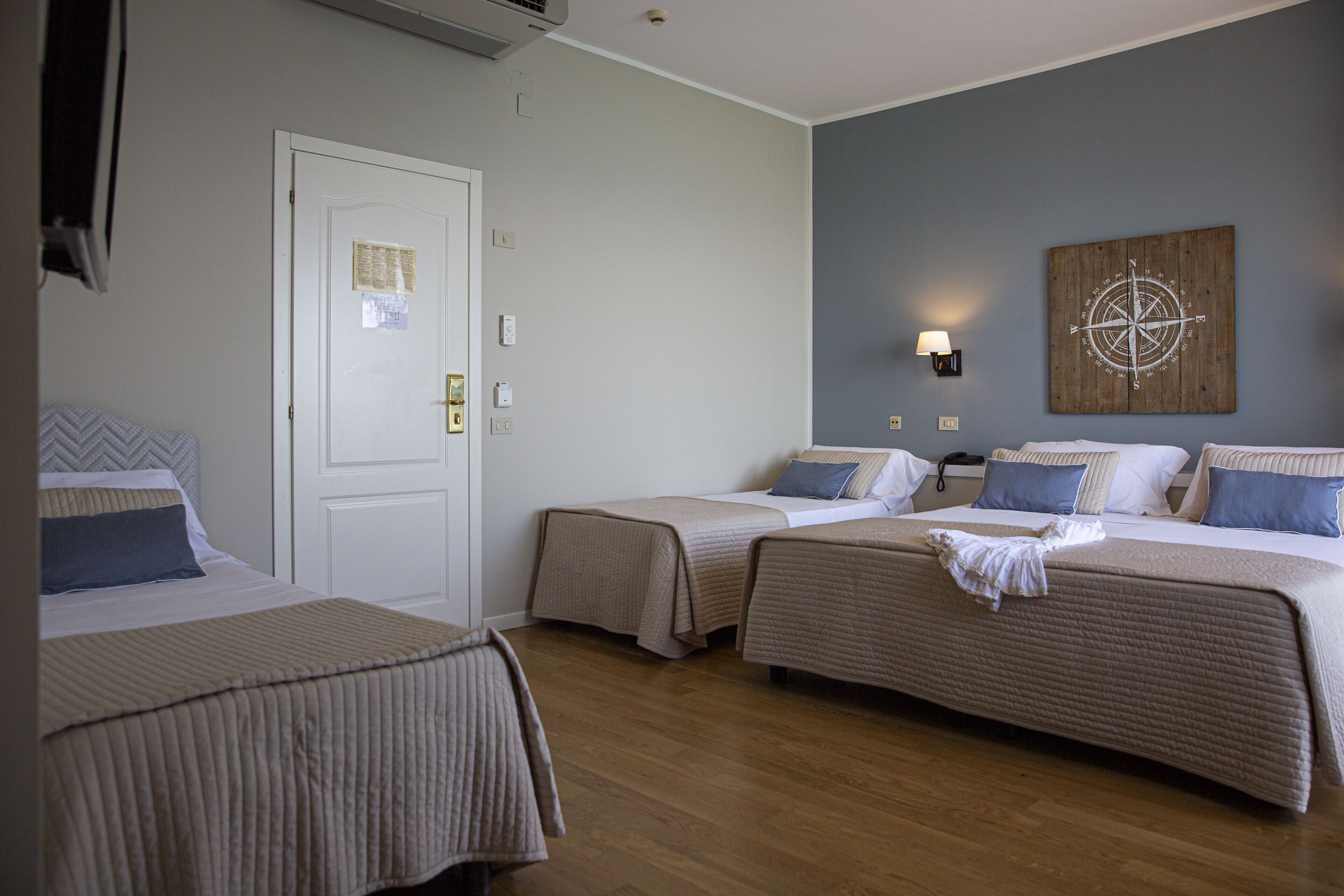 Ein Hotelzimmer mit zwei Einzelbetten, Holzboden, einer weißen Tür und einem an der Wand befestigten Kompass-Kunstwerk.