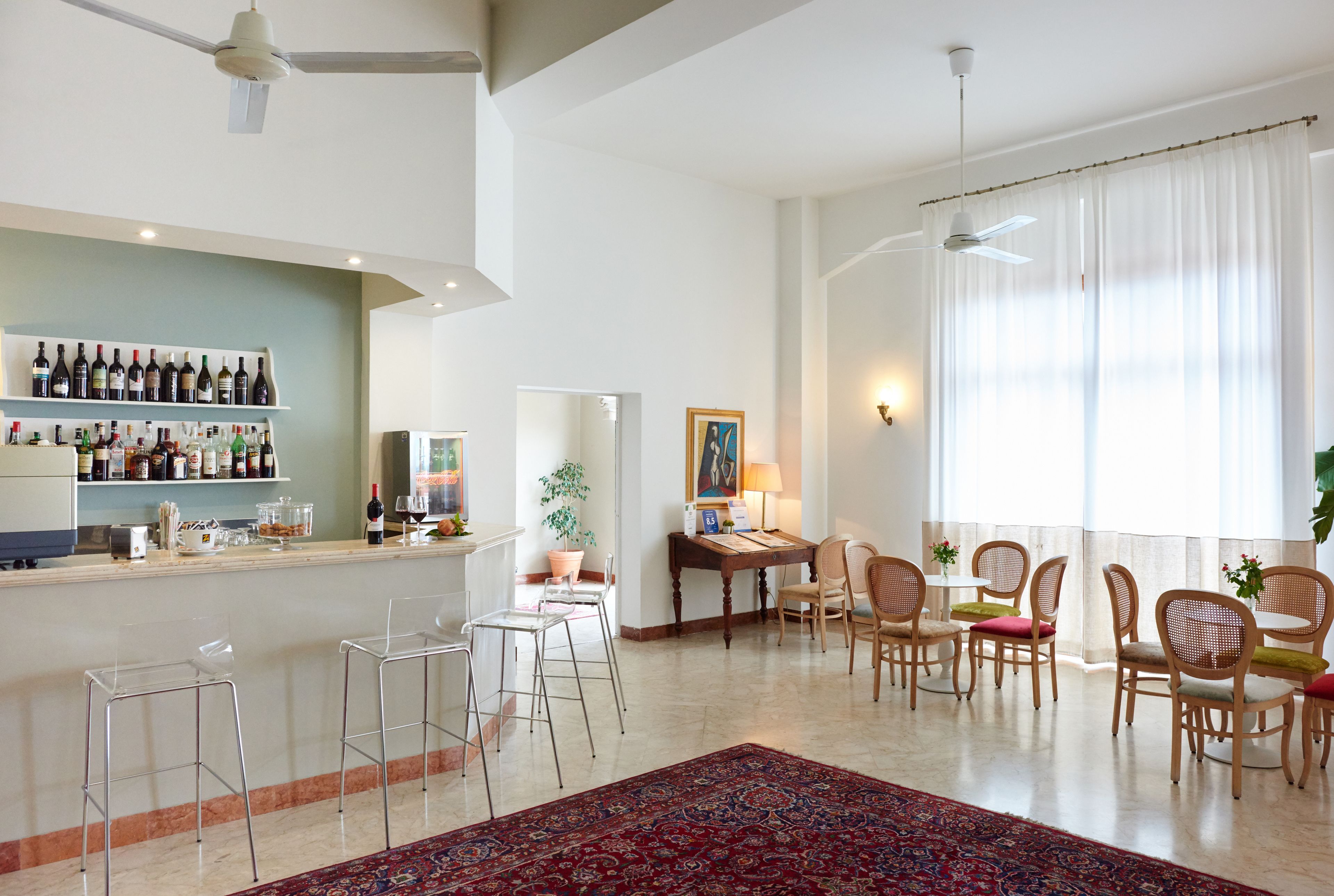 Una sala de estar moderna con una zona de bar, taburetes de bar transparentes, una mesa de comedor con sillas y un ventanal con cortinas.