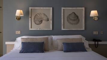 Uma cama com duas almofadas, uma parede com duas obras de arte com conchas emolduradas e duas luminárias fixadas na parede.