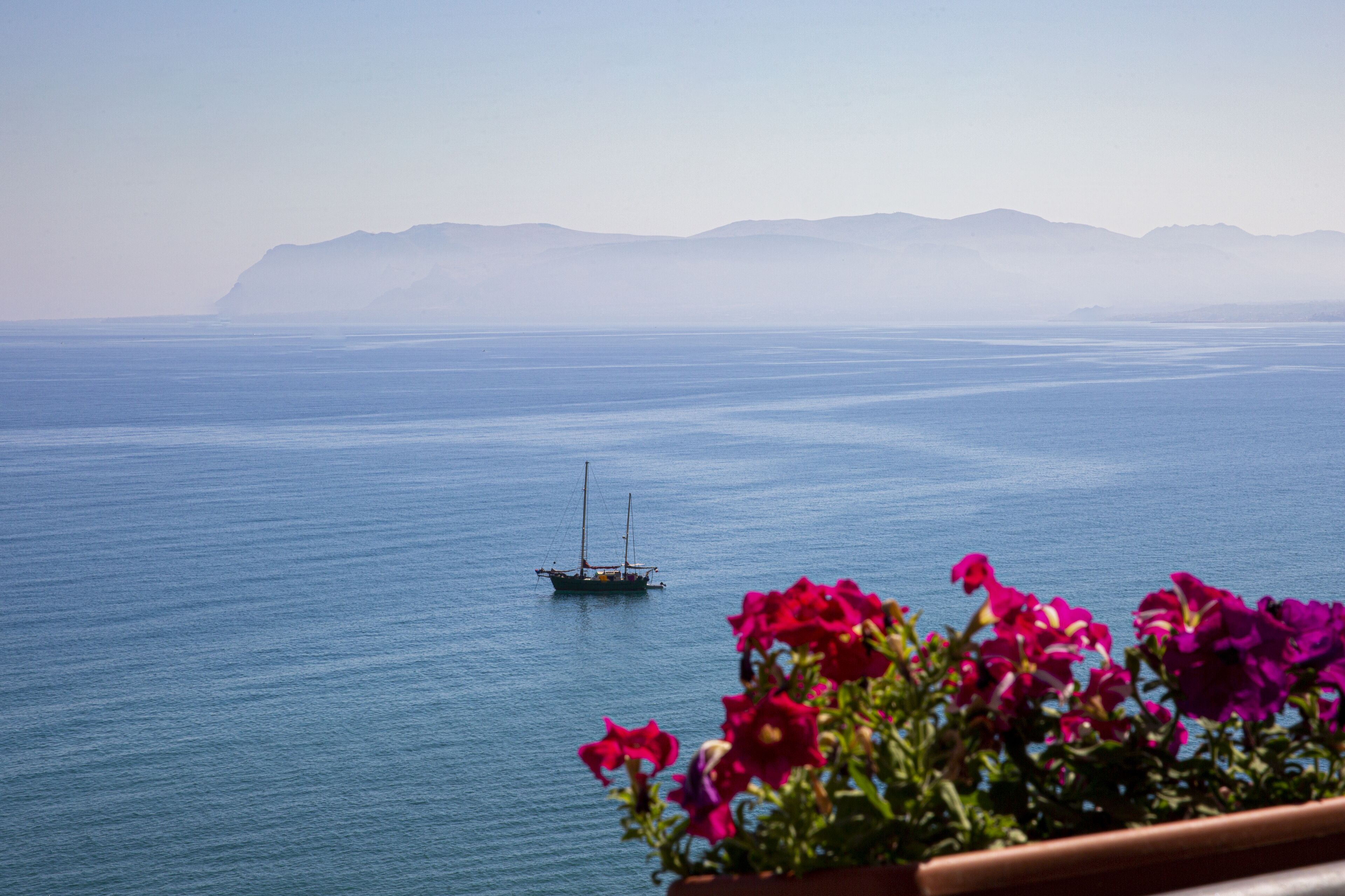 Vista de un mar tranquilo con un barco a lo lejos y montañas al fondo.