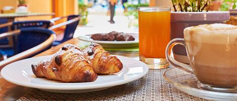 Un desayuno con croissants, un vaso de zumo de naranja y una taza de café sobre una mesa.