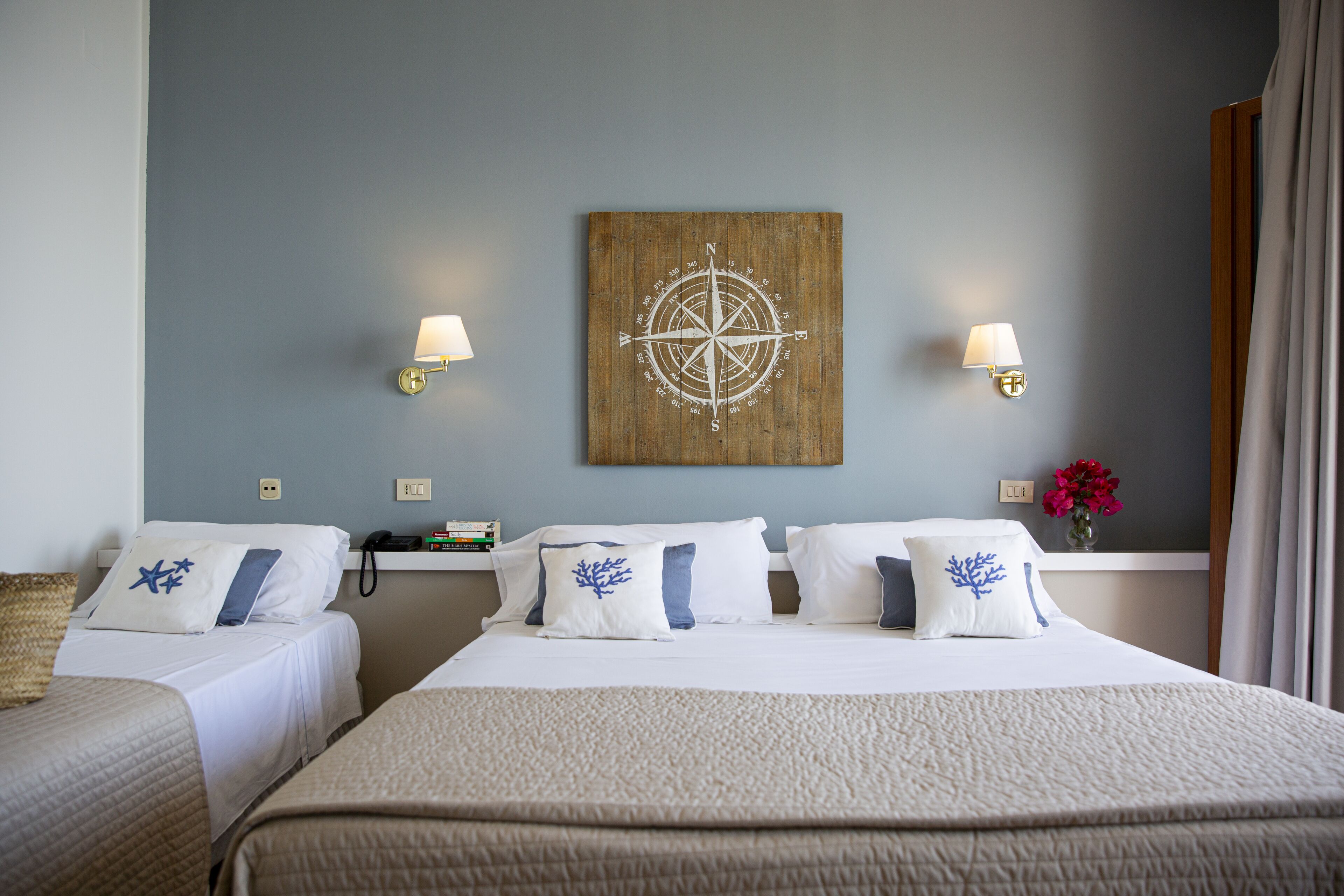A hotel room with two beds, a wooden wall art piece, bedside lamps, and a vase with flowers.