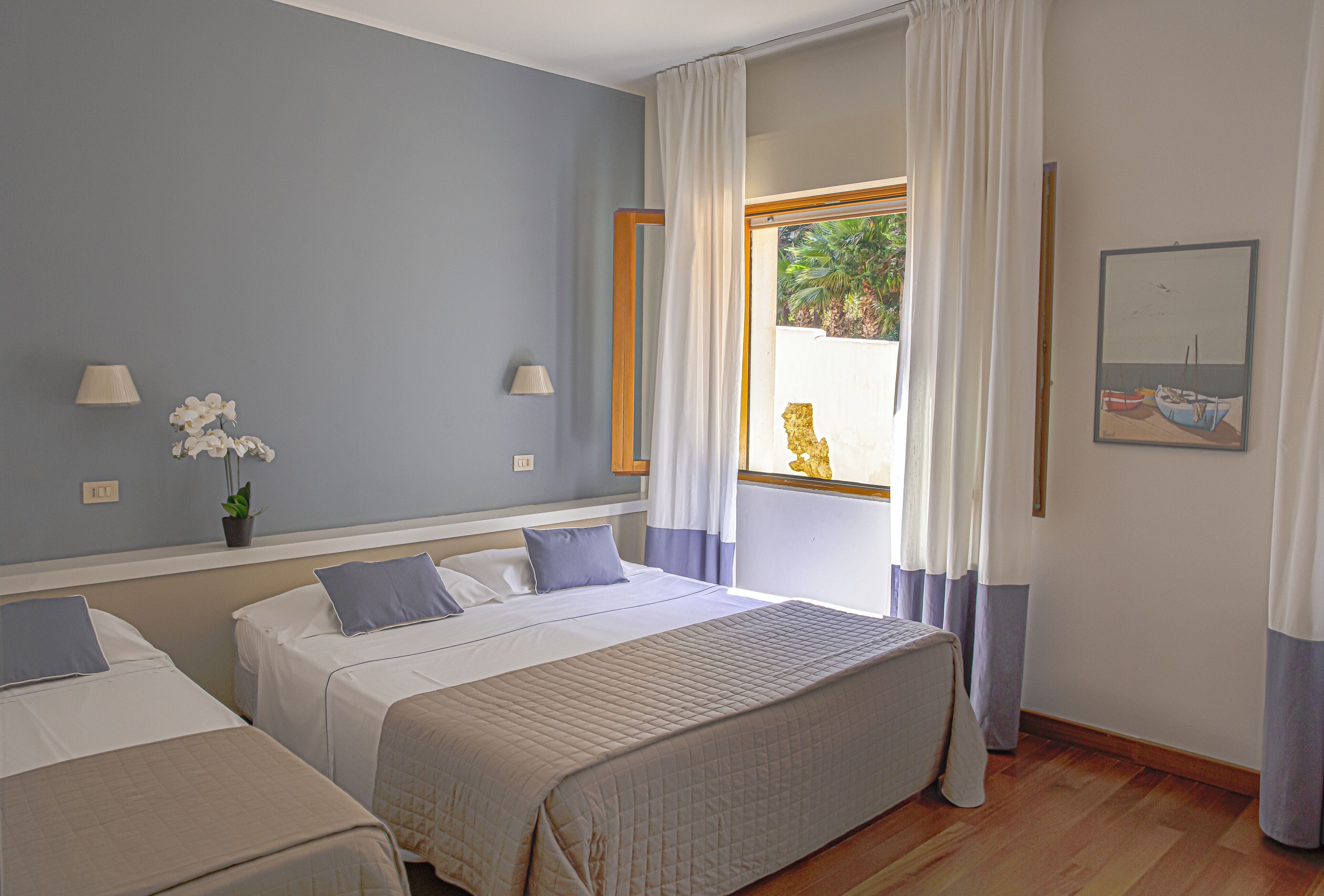 A hotel room with two beds, a window with curtains, a lamp, and a painting on the wall.