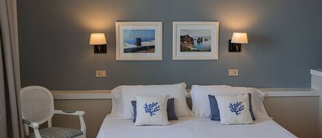 A hotel room with a bed, two wall-mounted lamps, two framed pictures, and a chair with a cushion.