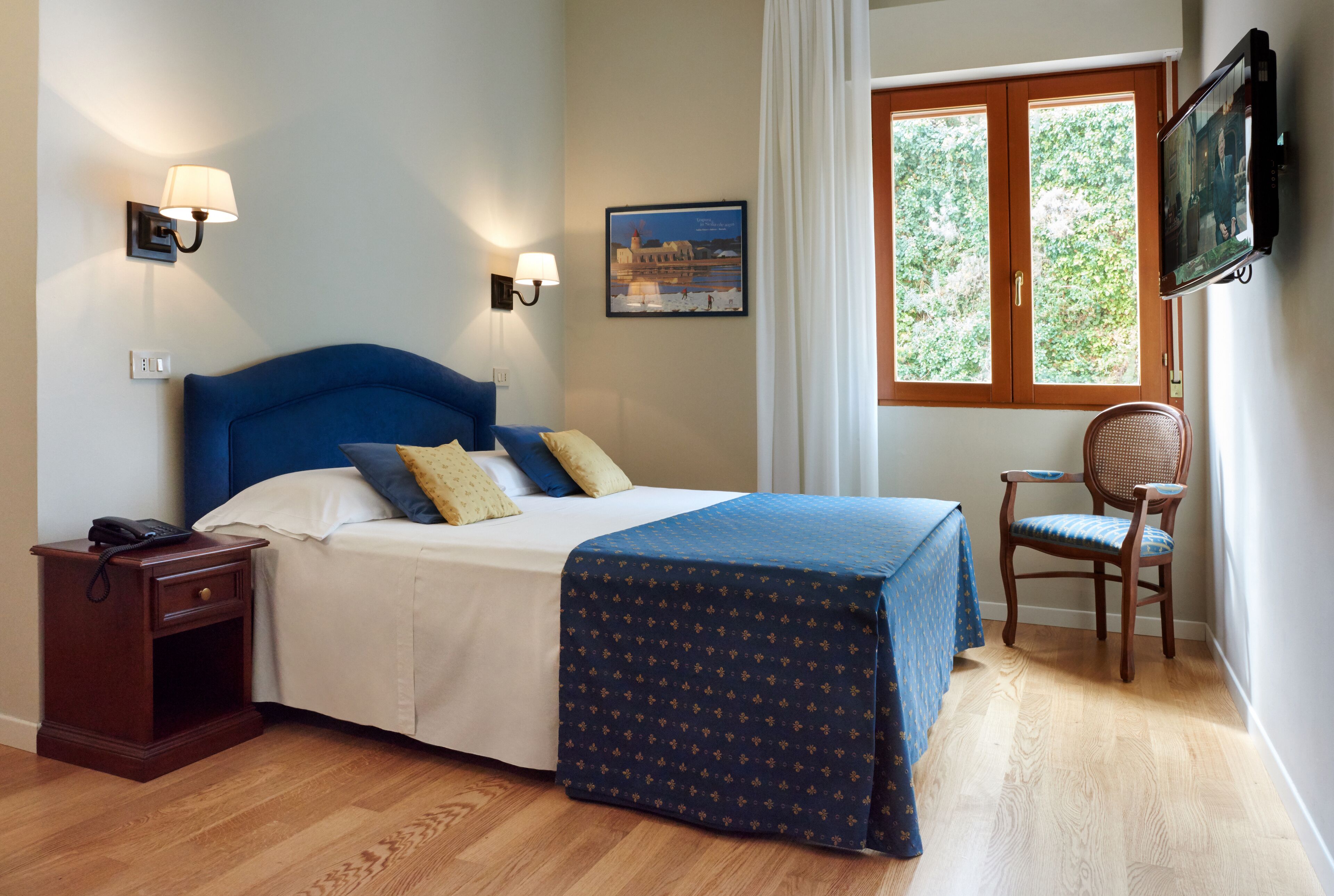 A neatly arranged bedroom with a bed, bedside lamps, a chair, a nightstand, and a window with curtains.