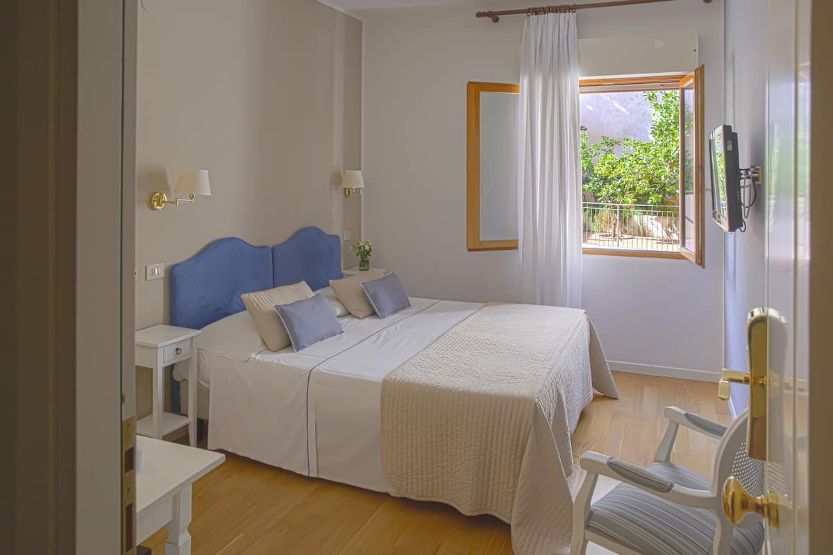 Un dormitorio con cama, mesitas de noche, una silla, ventana con vistas y un teléfono en la pared.