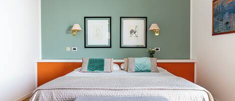A neatly arranged bedroom with a bed, two framed artworks on the wall, and a nightstand with a lamp.