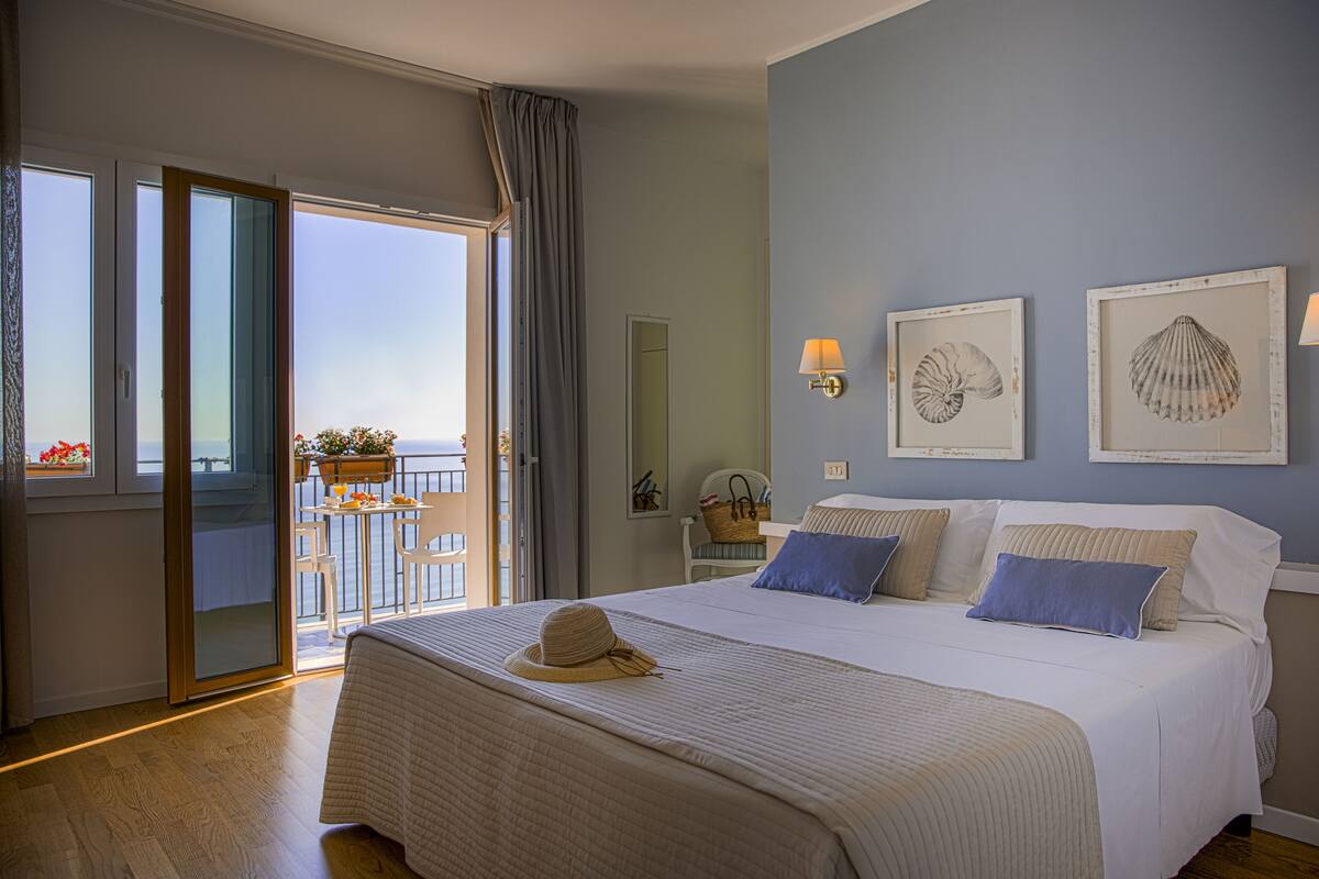 Una habitación de hotel con una cama grande, un balcón con vistas y dos cuadros enmarcados en la pared.