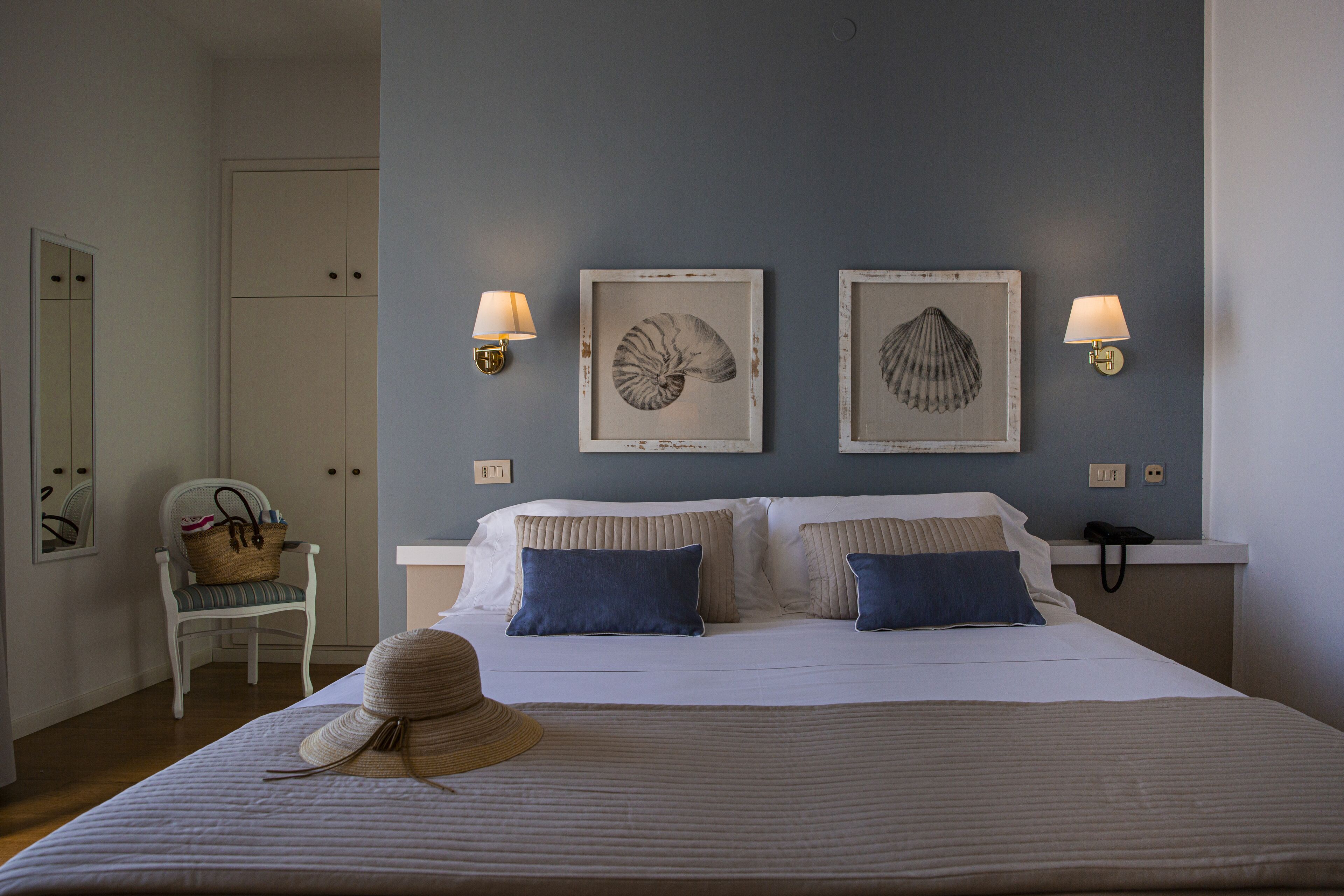 A neatly arranged bedroom with a bed, two wall-mounted lamps, and framed artwork on the wall.