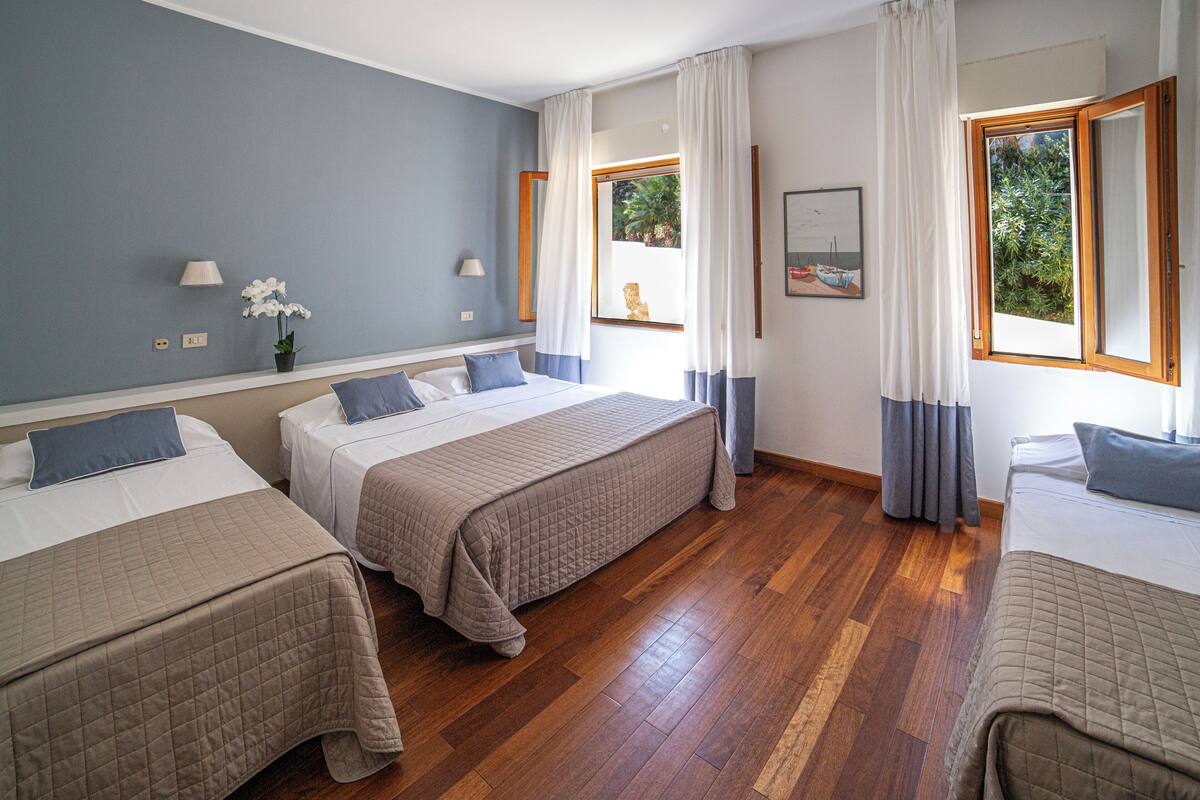 Una habitación de hotel con dos camas, una ventana con cortinas, una lámpara y un cuadro en la pared.