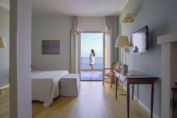 A hotel room with a bed, a desk, a chair, a TV, and a balcony with a view. - Hotel Punta Nord - Est (Castellammare del Golfo)