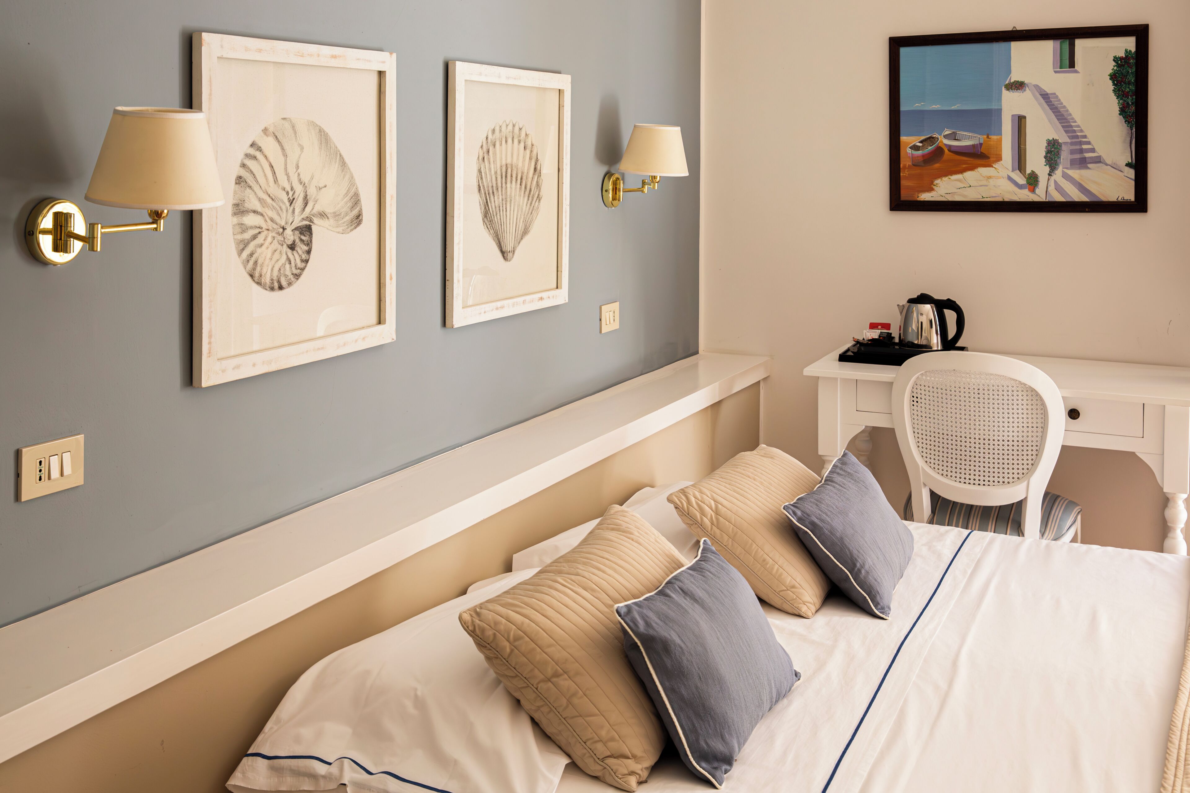 A bedroom with a bed, two wall-mounted lamps, and two framed artworks.