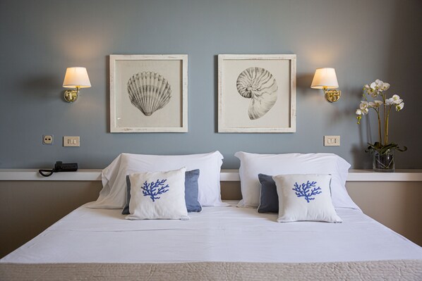 A hotel room with a bed, two wall-mounted lamps, and two framed shell artworks.