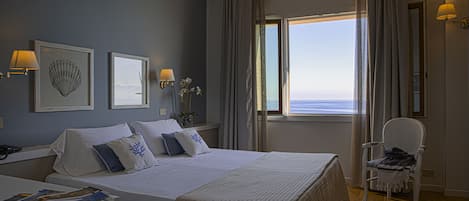 A hotel room with a large bed, a chair, a window with a view, and wall-mounted lamps.