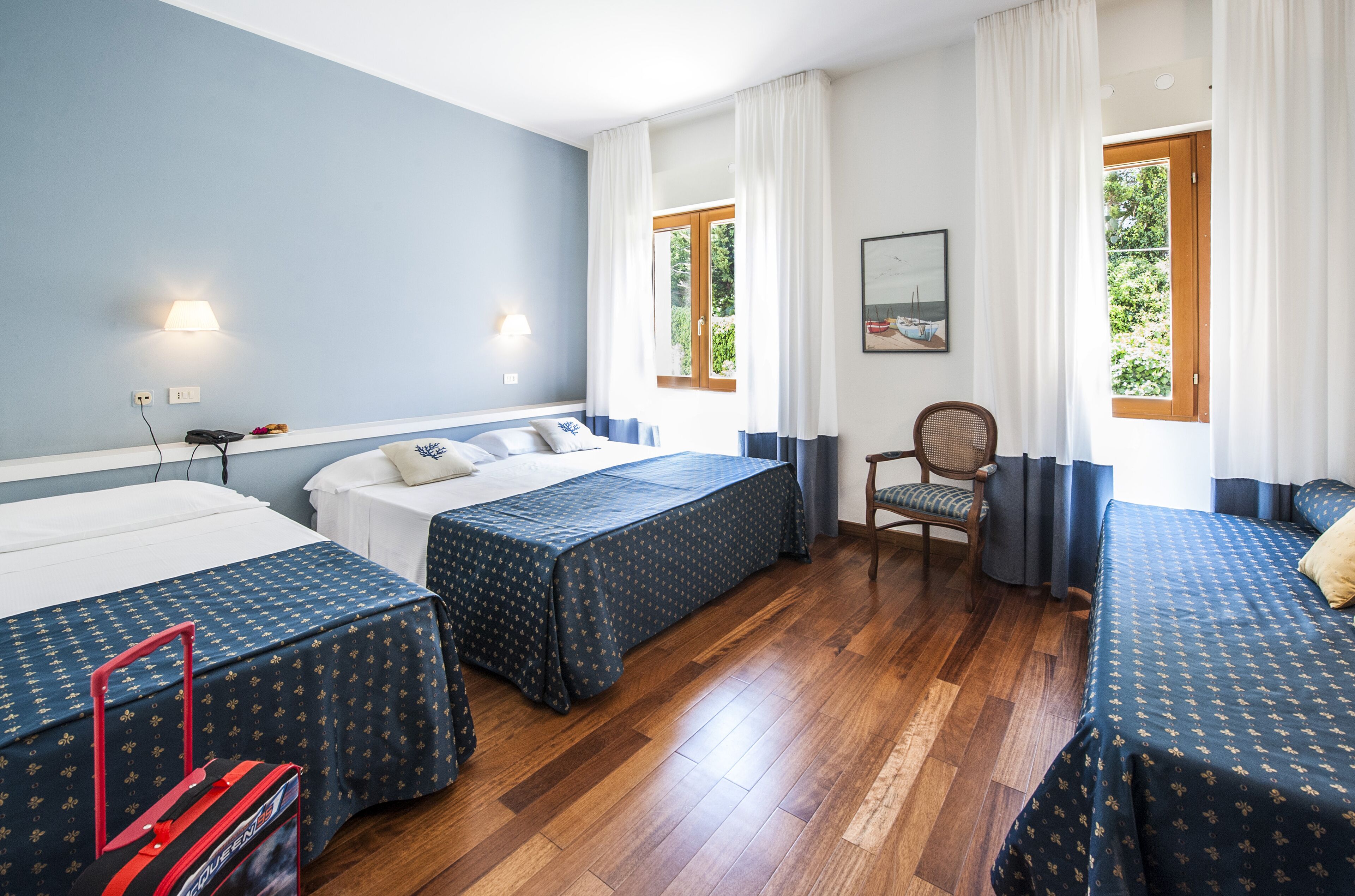 Quarto de hotel com duas camas, uma cadeira e uma janela com cortinas.