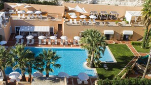 A rooftop pool area with sun loungers and umbrellas, a swimming pool, and palm trees.