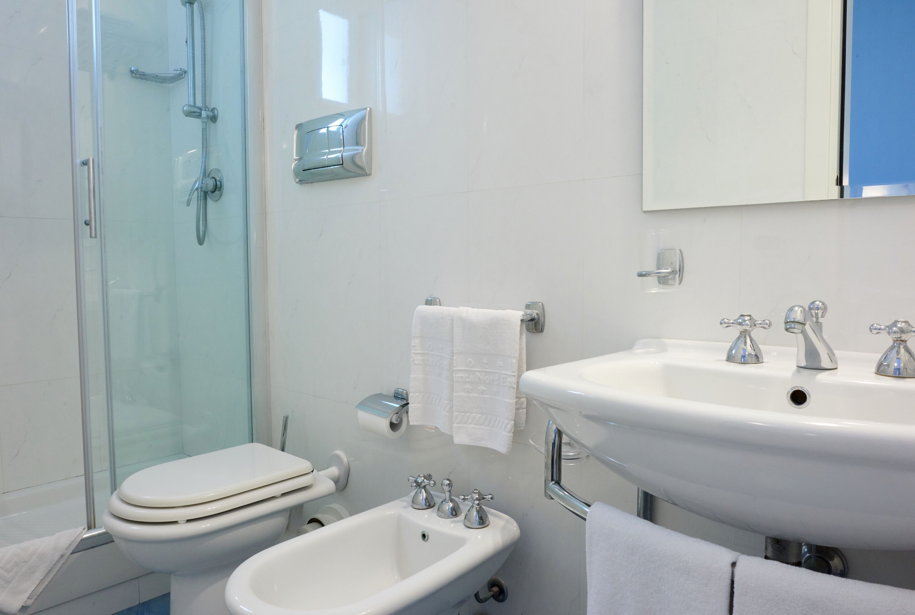 A bathroom with a glass-enclosed shower, a toilet, a bidet, and two sinks with faucets.
