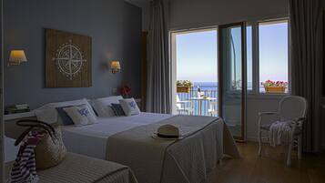 A hotel room with a large bed, two bedside tables, a chair, a balcony with a table and chairs, and a view of the sea.