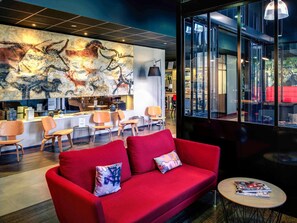 Un moderno vestíbulo de hotel con un sofá rojo, un mostrador de recepción y un mural de animales.