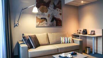 Ein modernes Hotelzimmer mit einer Couch, einem Couchtisch, einem Schreibtisch mit Kaffeemaschine und einem Bild an der Wand.