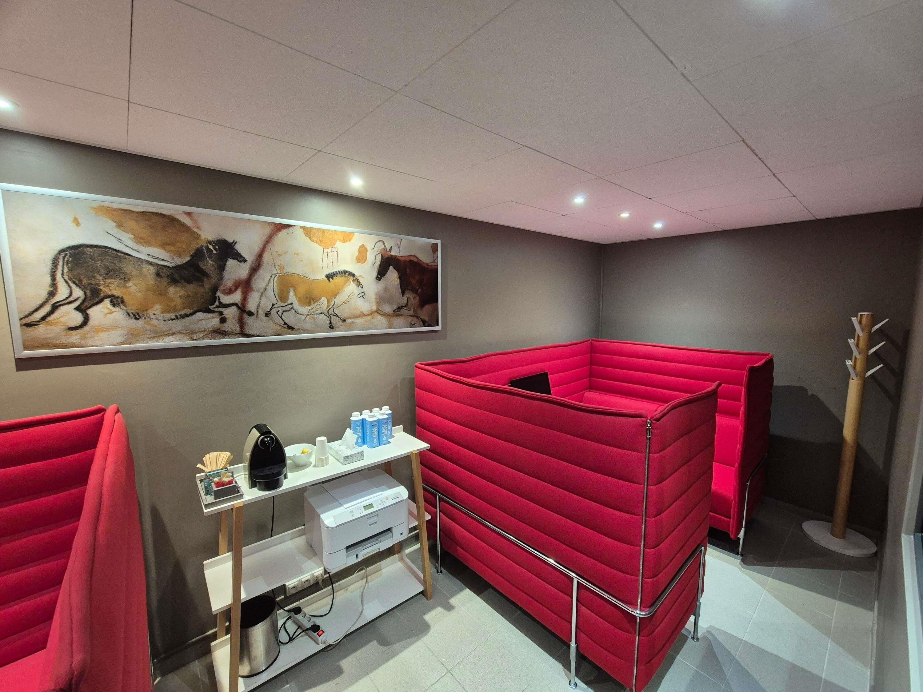 Une pièce avec un coin salon doté de sièges rembourrés rouges, un bureau blanc avec une imprimante et un grand tableau représentant des chevaux accroché au mur.