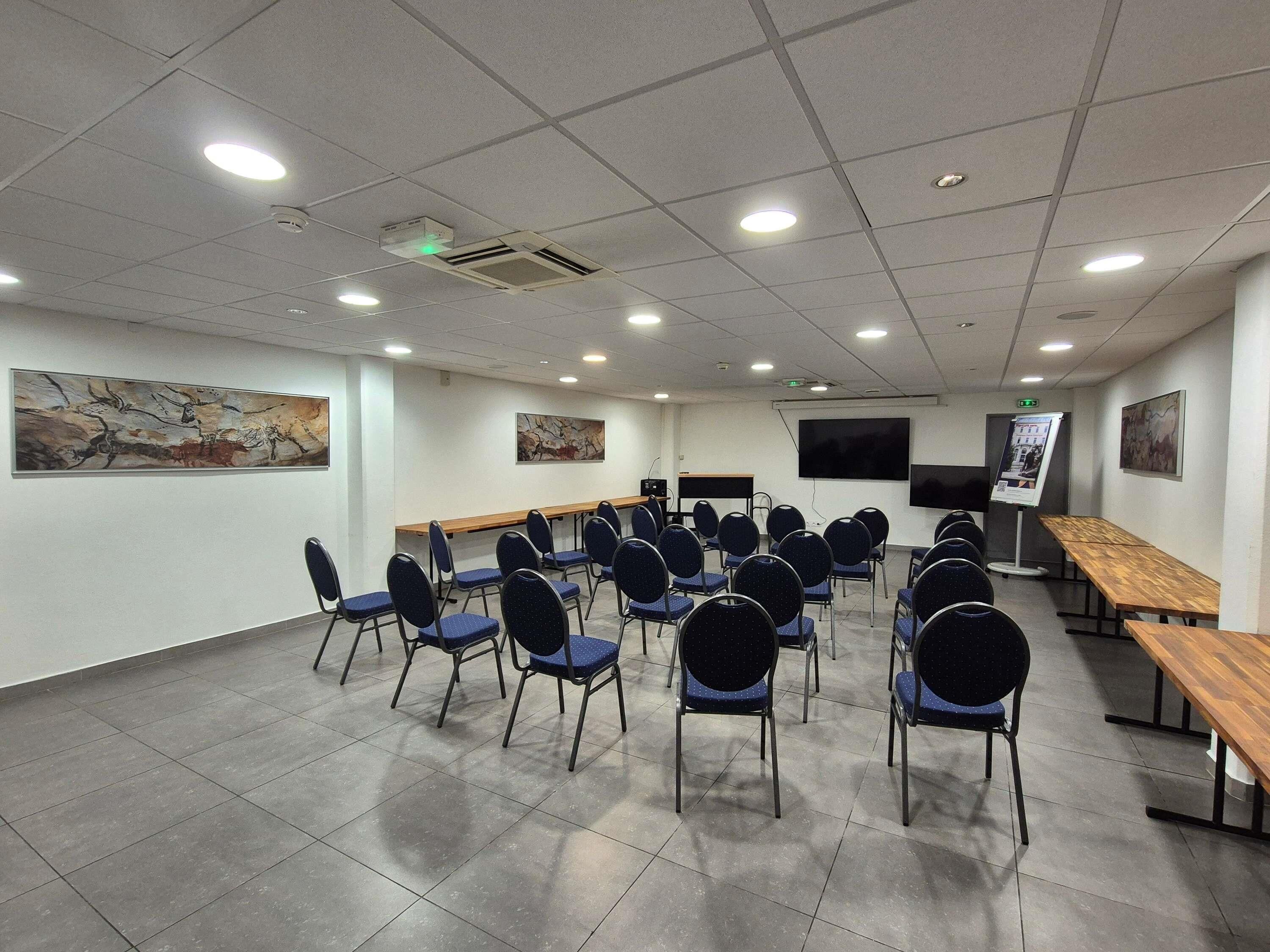 Un salón de conferencias con una larga mesa, sillas, un proyector y una pantalla.