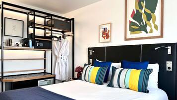 Habitación de hotel con cama, mesita de noche, estante empotrado, bata y cuadros en la pared.