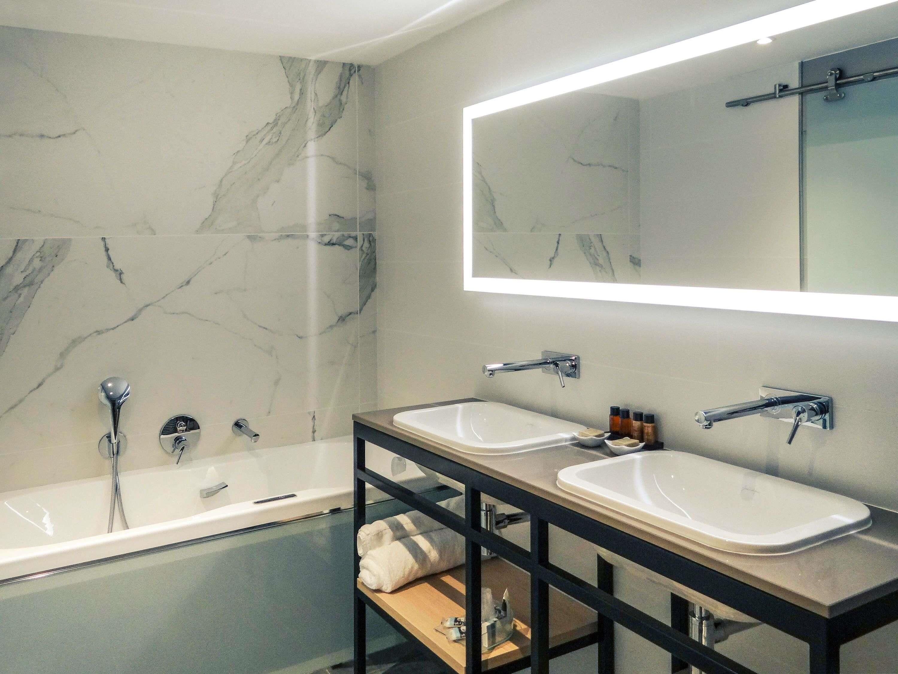 Un baño moderno con pared de mármol, un espejo grande, una bañera y dos lavamanos.