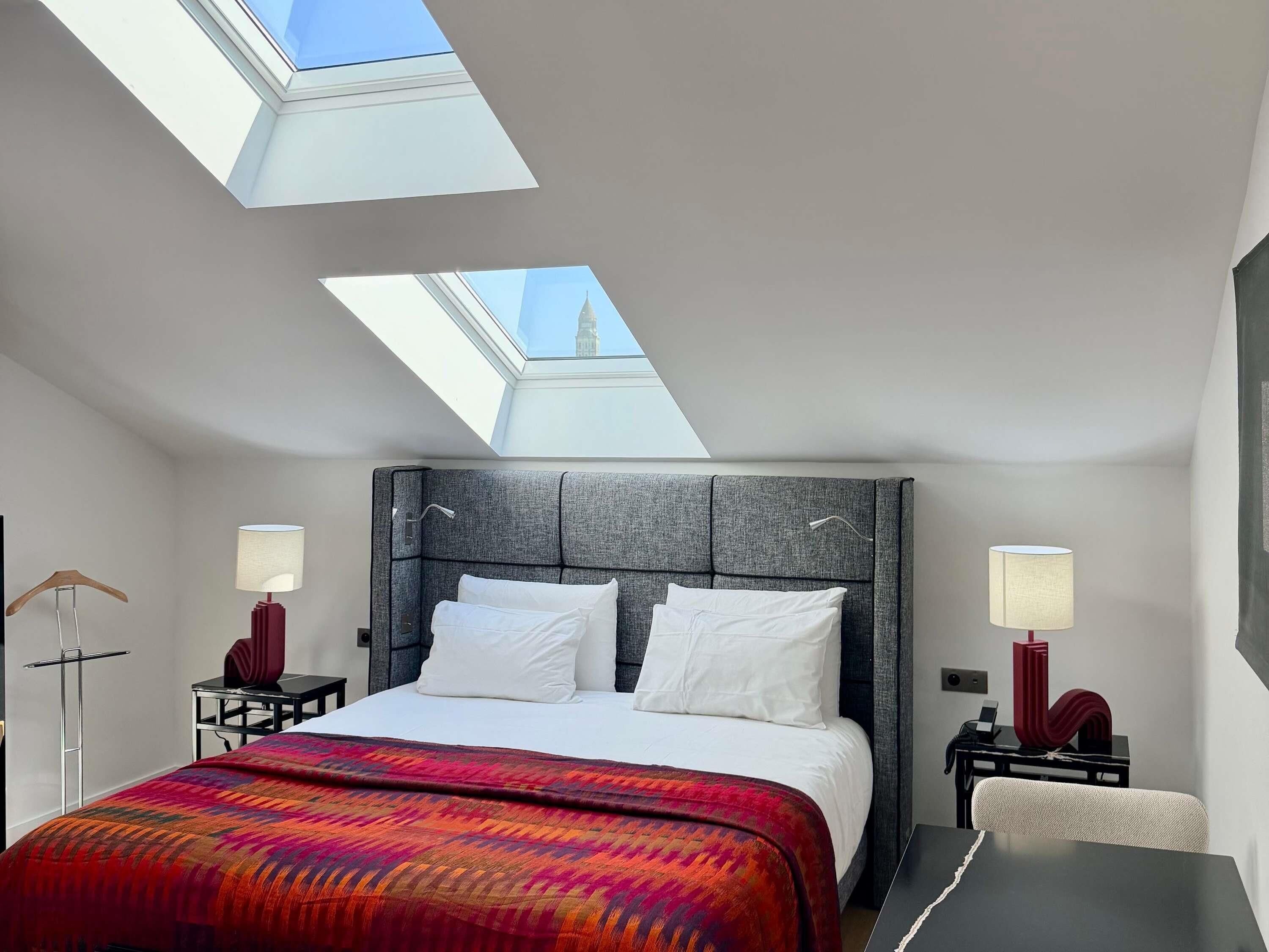 Une chambre d’hôtel moderne avec un grand lit, des fenêtres de toit et une vue sur une tour.