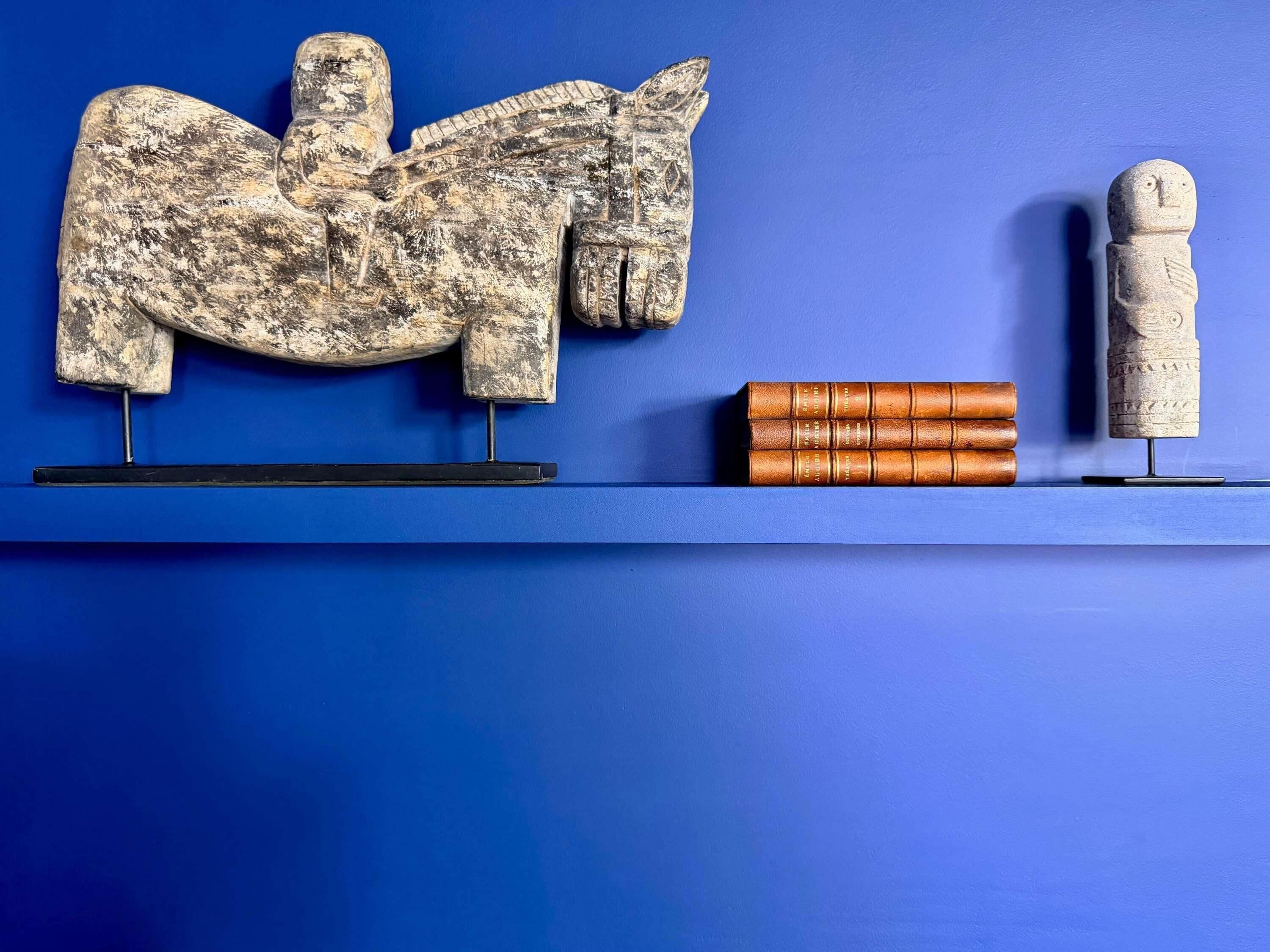 Eine blaue Wand mit einem angebrachten Skulpturenpaar: ein Pferd und eine kleine Statue.