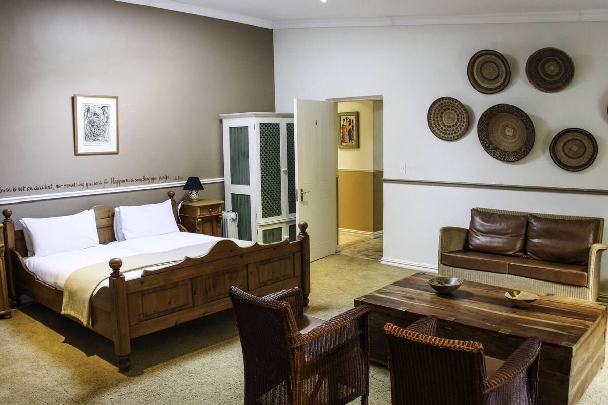 Une chambre à coucher avec un lit en bois, des fauteuils en osier, une table basse en bois et un canapé.