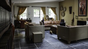 Ein geräumiges Wohnzimmer mit einer großen Couch, zwei Sesseln und einem Couchtisch. Im Hintergrund steht ein Klavier, und der Boden ist mit Fliesen belegt.