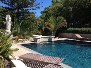 Una piscina con cubierta de madera, rodeada de palmeras y una estructura de piedra.