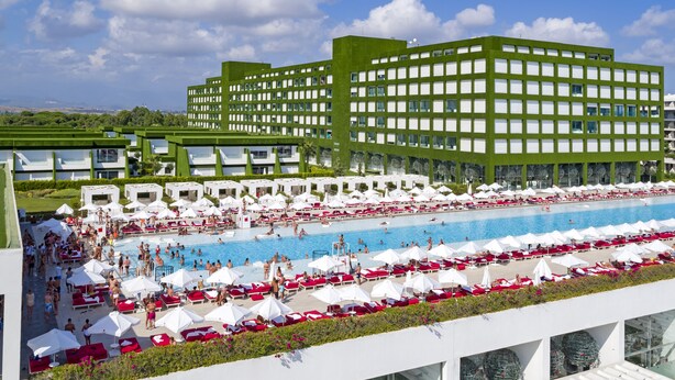 Ein modernes Hotel mit großzügiger Poolanlage, mehreren Schwimmbecken und zahlreichen Liegestühlen und Sonnenschirmen.