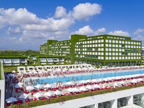 A modern hotel with a large pool area, multiple swimming pools, and numerous sun loungers and umbrellas.
