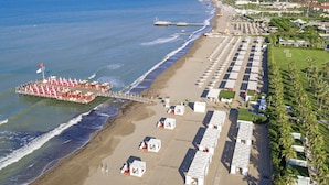 Eine Vogelperspektive eines Strandraumes mit einer Pier, Strandsonnenschirmen und Strandhütten.
