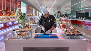Ein Koch bereitet Essen in einer modernen, gut beleuchteten Küche zu, auf den Arbeitsflächen sind verschiedene Gerichte angerichtet.