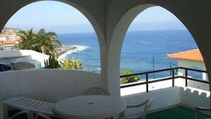 Varanda com vista para o oceano, com mesa, cadeiras e um pequeno espaço de estar.