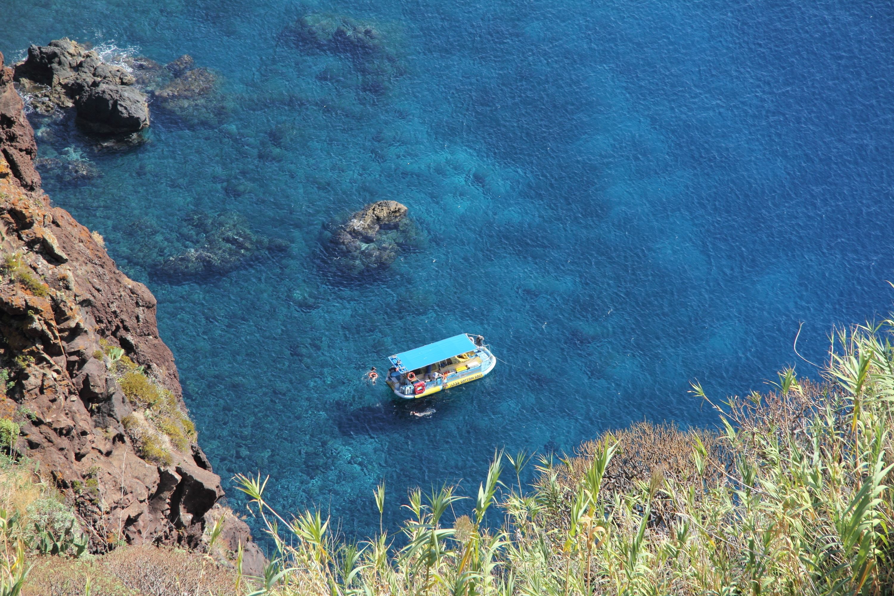 Un bateau sur une eau d’un bleu limpide, entouré de falaises rocheuses et de végétation.