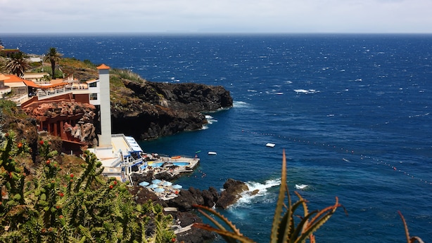 Um hotel à beira-mar com área de piscina, uma torre branca imponente e falésias rochosas com vista para o mar.
