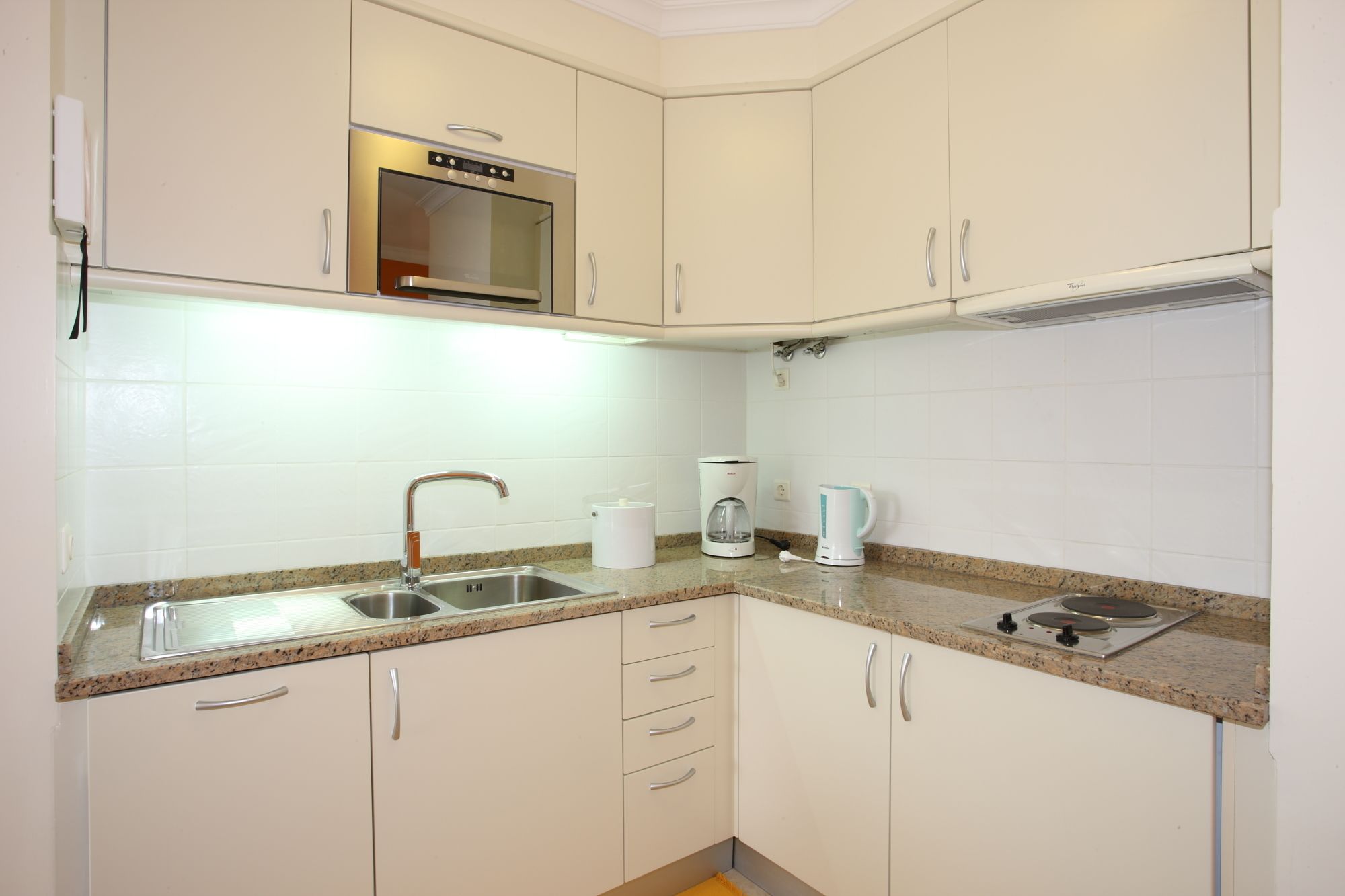 A kitchen with white cabinets, a stainless steel sink, a microwave, a coffee maker, and a gas stove.