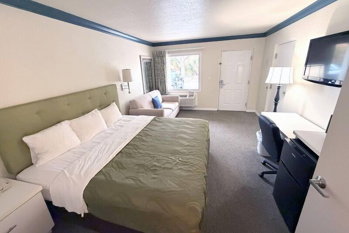A hotel room with a bed, a desk, a chair, a TV, and a window with curtains.