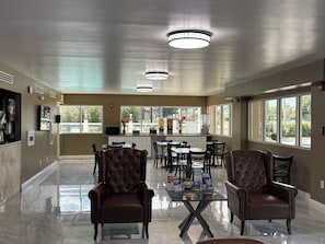 A spacious indoor area with a kitchen counter, seating arrangements, and large windows.