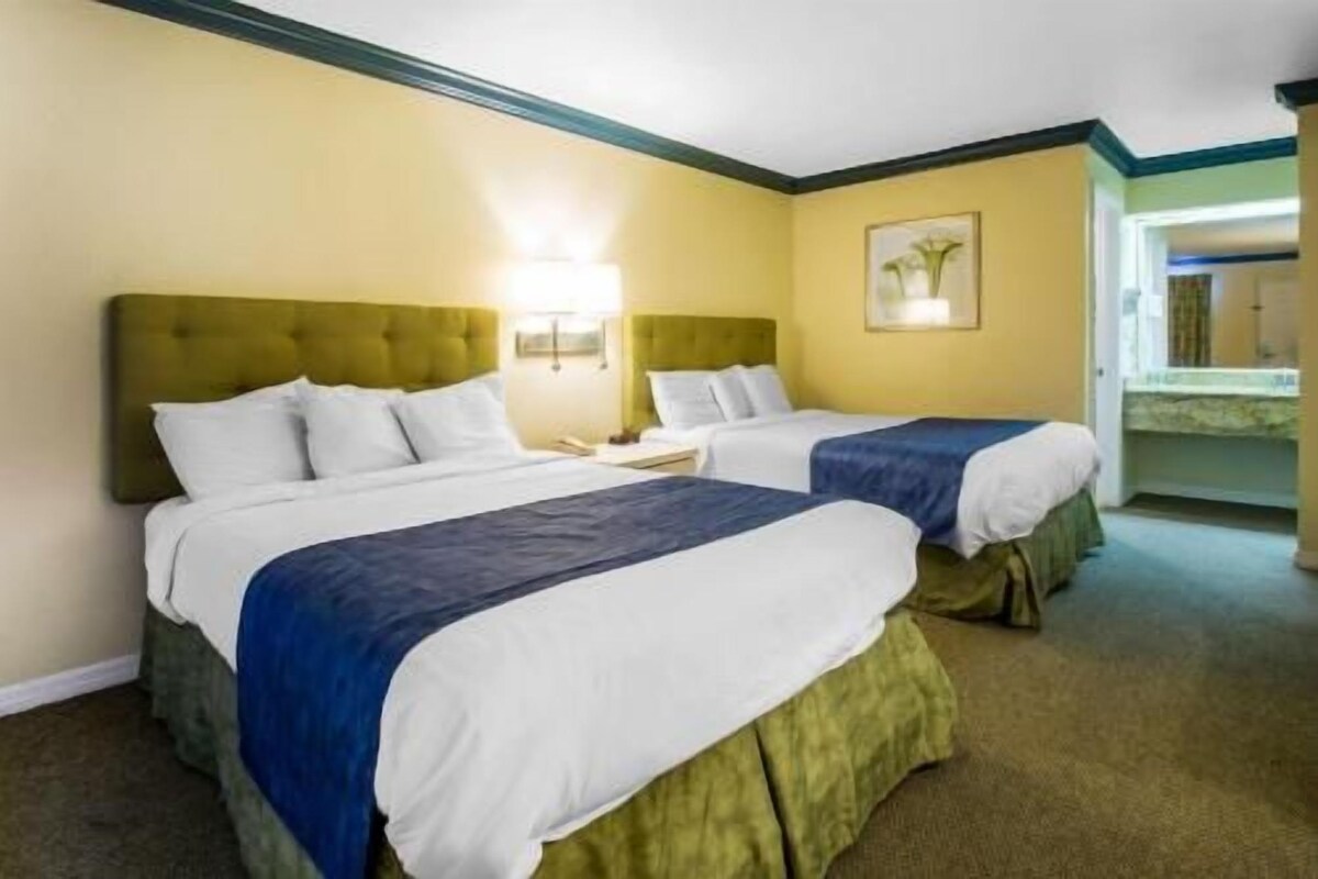 Hotellihuone, jossa on kaksi sänkyä, yöpöytä ja peili.
