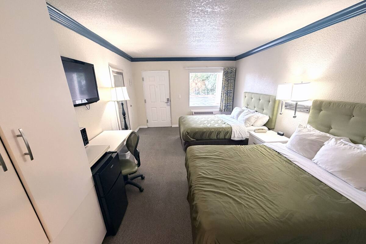 A hotel room with two beds, a desk with a chair, a television, and a door.