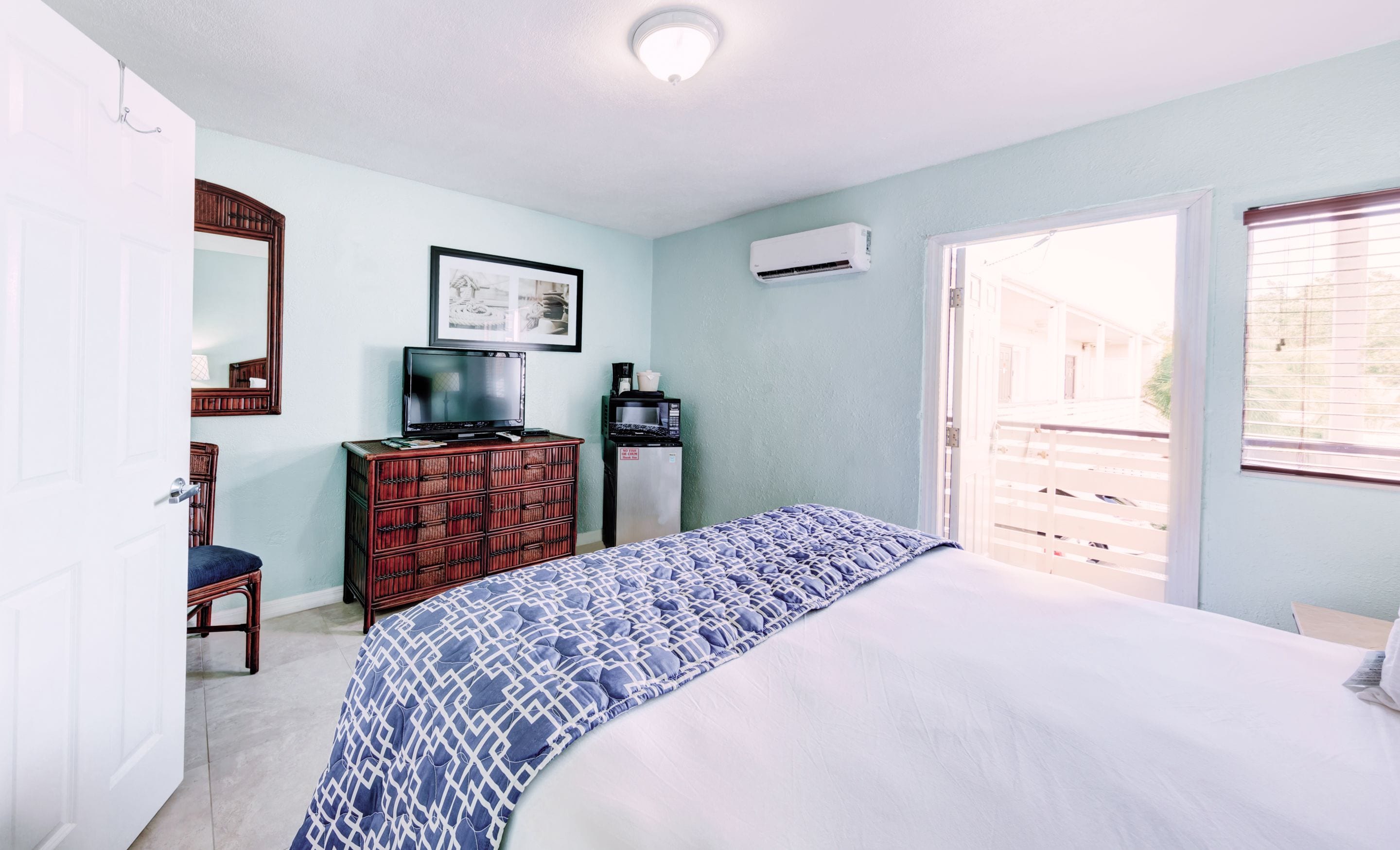 A bedroom with a bed, dresser, television, and air conditioning unit.