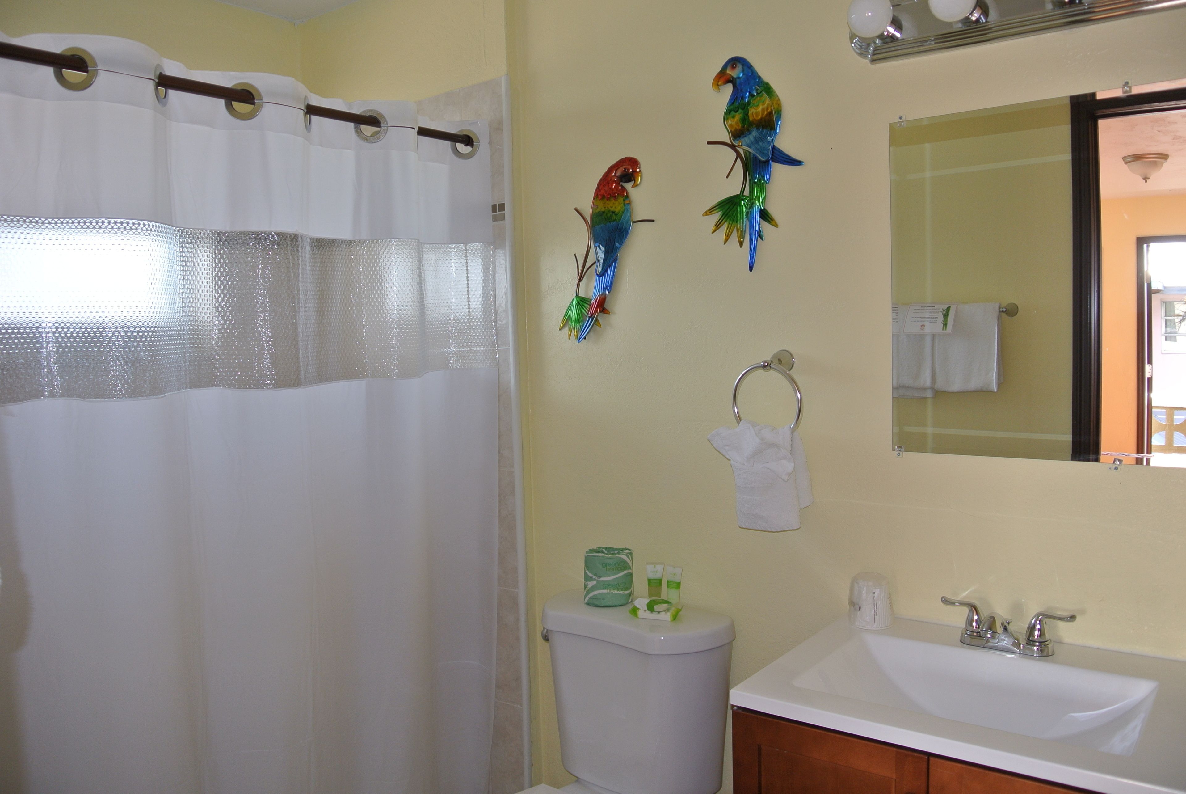 Ein Badezimmer mit Duschvorhang, Toilette, Waschbecken und zwei Vogelzierdekorationen an der Wand.