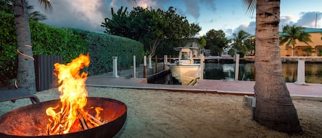 A fire pit with flames, a body of water, and a boat docked nearby.