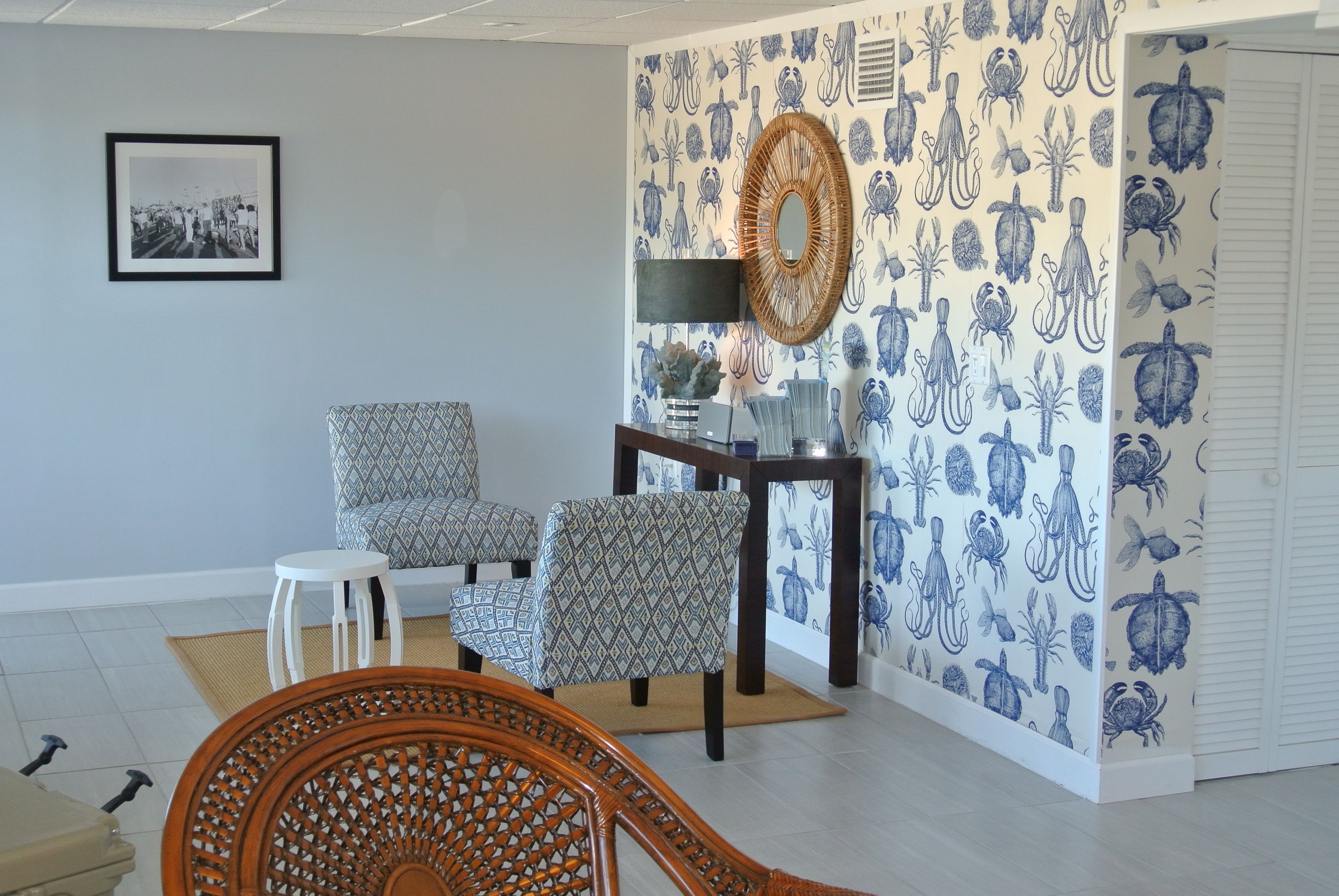 Un salón con papel tapiz estampado, un cuadro enmarcado y un sillón de mimbre.