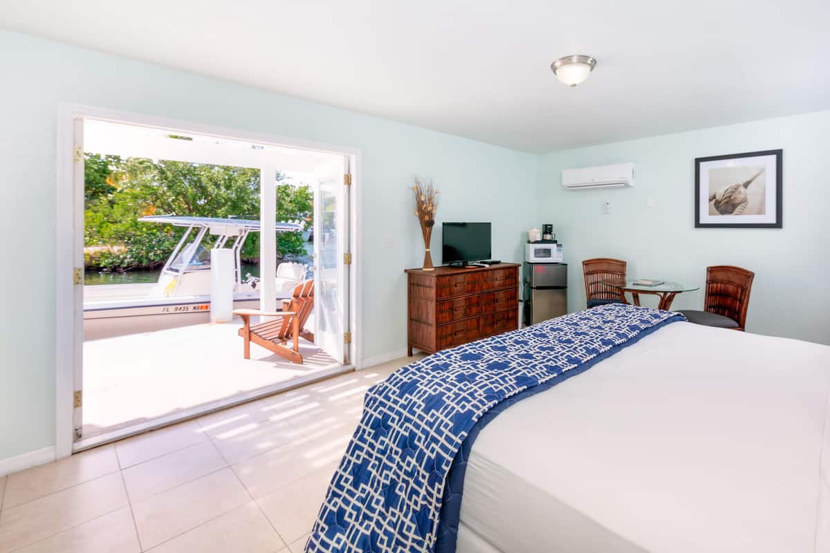 Une chambre d’hôtel avec un lit, un bureau et une chaise, une petite table et une vue sur un bateau et la verdure environnante.